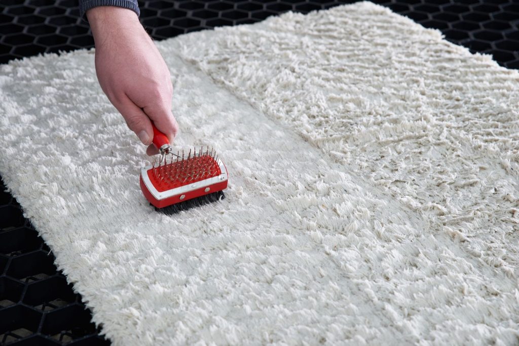 a person using a red grooming brush to clean a white shag rug